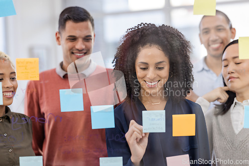 Image of Black woman, writing and schedule planning with team in strategy or brainstorming on glass wall at office. African American female designer in teamwork project plan, tasks or post it with sticky note