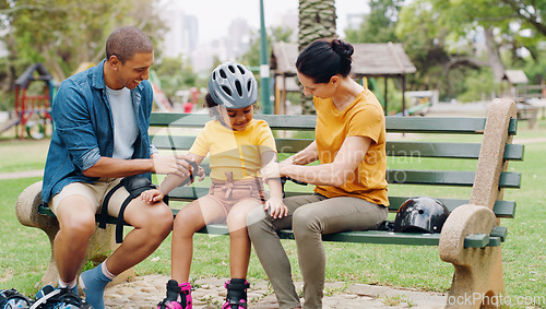 Image of Parents, park bench and helmet with kid, help and safety for skating, rollerskate or bike. Interracial family, mom and dad with helping hand, teaching and girl kid for bonding, learning and exercise