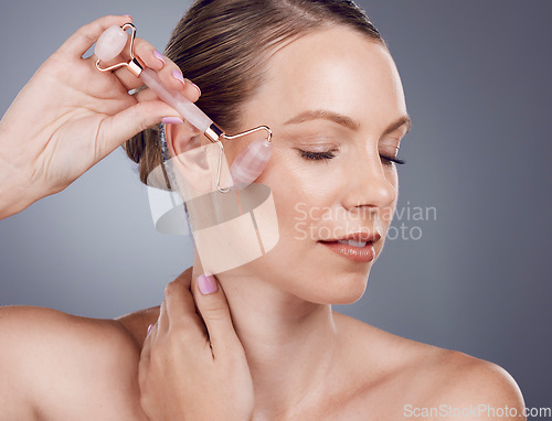 Image of Rose quartz, facial massage and woman with face roller for wellness, dermatology and skincare. Isolated, gray background and model with beauty for facelift and self care with crystal in studio
