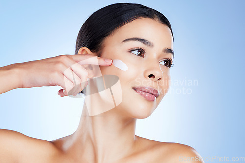 Image of Woman, face and hand for skincare moisturizer in cosmetics or beauty against a blue studio background. Female applying product, lotion or cream for facial treatment, collagen or healthy self care