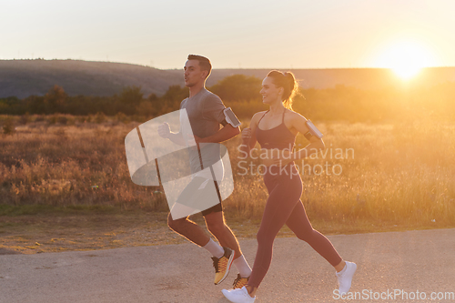 Image of A handsome young couple running together during the early morning hours, with the mesmerizing sunrise casting a warm glow, symbolizing their shared love and vitality