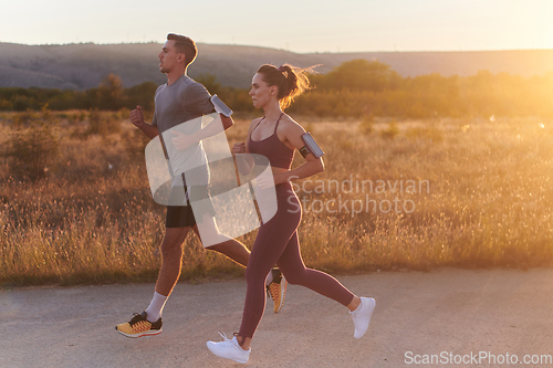 Image of A handsome young couple running together during the early morning hours, with the mesmerizing sunrise casting a warm glow, symbolizing their shared love and vitality