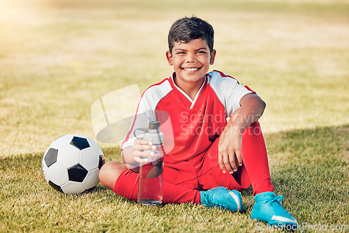 Image of Soccer, children and water with a ball and boy child sitting on a grass pitch or field after training. Football, fitness and hydration with a young male kid at a sports venue, stadium or arena