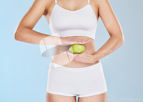 Image of Health, weight loss and apple on stomach of woman in underwear for nutrition, diet and vegan lifestyle. Wellness, fitness and digestion with hands of girl and fruit on slim body with blue background