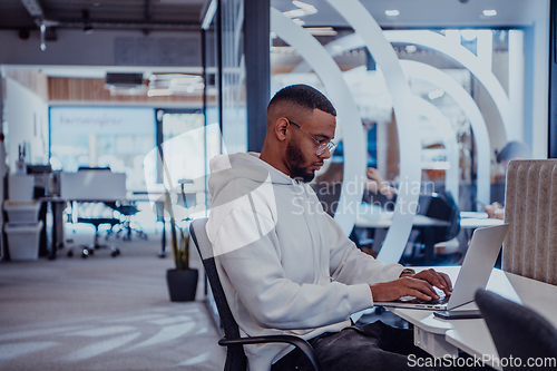 Image of In a modern office setting, an African American businessman is diligently working on his laptop, embodying determination, ambition, and productivity in his professional environmen