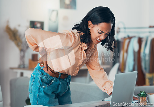 Image of Back pain, discomfort and tired designer working on a laptop in a clothing boutique or store. Young overworked business owner, shop assistant suffering from injury, backache and pain at desk