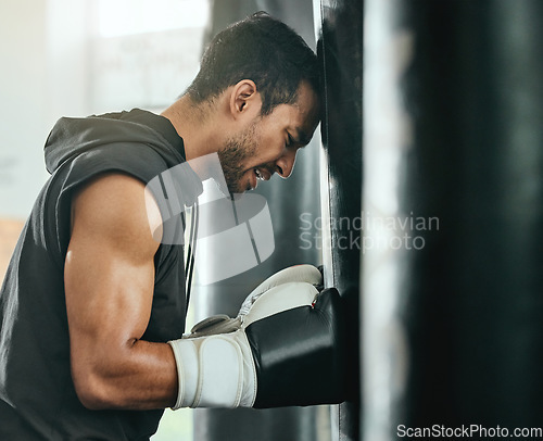 Image of Strong, sweaty and fit male boxer resting while doing a cardio workout with a punching bag at gym. Sporty, active and determined athlete looking tired while exercising at a sports center for fitness.