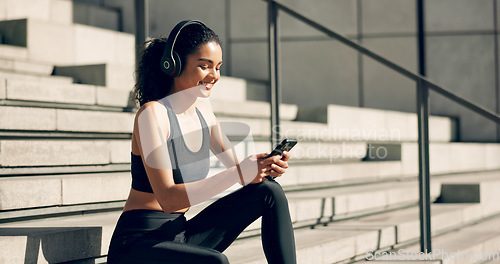 Image of Runner woman, headphones and phone on stairs with music, smile and relax in city, workout and training. Girl, smartphone and happy with audio streaming subscription with typing, social media or app