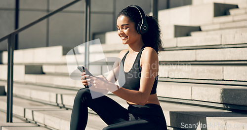 Image of Runner girl, headphones and phone on stairs with music, smile and relax in city, workout and training. Woman, smartphone and sitting with audio streaming subscription with typing, social media or app