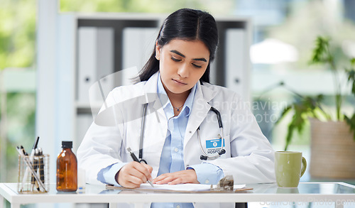 Image of Doctor writing a prescription or recommending medication letter while sitting at her desk. Professional female GP, surgeon or physician writing a medical file and report in clinic alone in a office