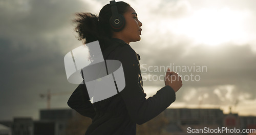 Image of Exercise, music and a sports woman running in the city for health or cardio preparation of a marathon. Fitness, wellness or training and a young runner or athlete listening to audio with headphones