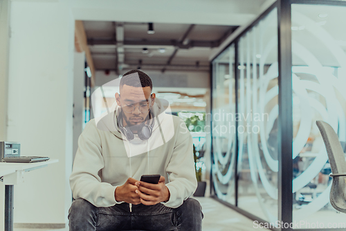 Image of African American businessman wearing headphones while using a smartphone, fully engaged in his work at a modern office, showcasing focus, productivity, and contemporary professionalism