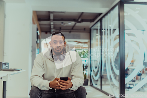 Image of African American businessman wearing headphones while using a smartphone, fully engaged in his work at a modern office, showcasing focus, productivity, and contemporary professionalism