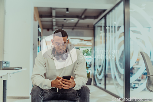 Image of African American businessman wearing headphones while using a smartphone, fully engaged in his work at a modern office, showcasing focus, productivity, and contemporary professionalism