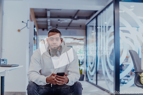 Image of African American businessman wearing headphones while using a smartphone, fully engaged in his work at a modern office, showcasing focus, productivity, and contemporary professionalism