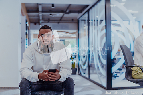 Image of African American businessman wearing headphones while using a smartphone, fully engaged in his work at a modern office, showcasing focus, productivity, and contemporary professionalism