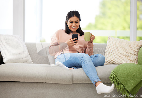 Image of Rest, relaxation and carefree with a young woman typing on a phone, drinking coffee and comfortable on the sofa at home. Relaxed female browsing social media or typing a message with a cup of tea