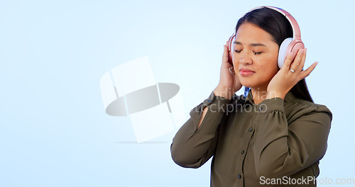 Image of Woman, headphones and listening to music or podcast, audio and song in studio by blue background. Asian female model, hearing and streaming radio, sound and playlist for peace, chilling and mockup