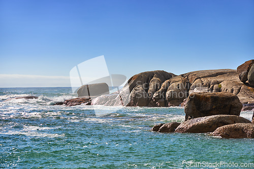 Image of Scenic view of nature, rocks and calm ocean water on a sunny day in Summer, with a beautiful blue sky in the background. Sea waves breaking close to the shore of the beach.