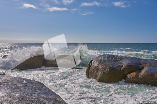 Image of A beautiful coastline with waves and rocks in the sea on a sunny, beach day. An ocean view of the water and a blue sky background in summer. Outdoor scenery of a relaxing seaside landscape in nature.