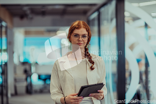 Image of A young business woman with orange hair self-confident, fully engaged in working on a tablet, exuding creativity, ambition and a lively sense of individuality