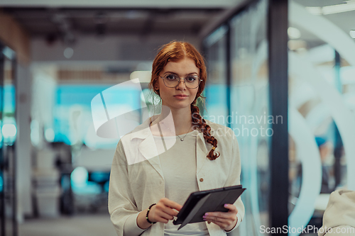 Image of A young business woman with orange hair self-confident, fully engaged in working on a tablet, exuding creativity, ambition and a lively sense of individuality