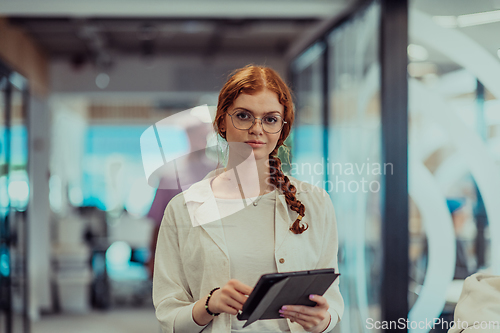 Image of A young business woman with orange hair self-confident, fully engaged in working on a tablet, exuding creativity, ambition and a lively sense of individuality