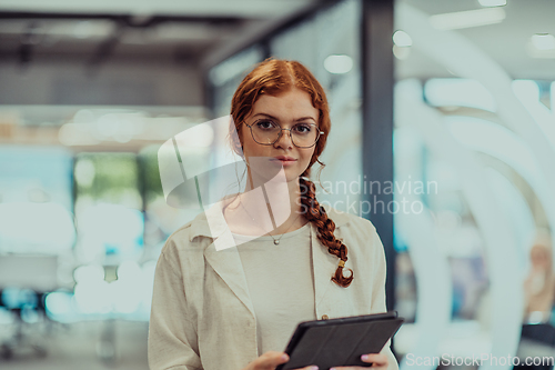 Image of A young business woman with orange hair self-confident, fully engaged in working on a tablet, exuding creativity, ambition and a lively sense of individuality