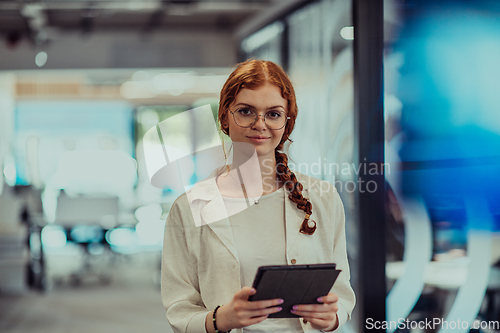 Image of A young business woman with orange hair self-confident, fully engaged in working on a tablet, exuding creativity, ambition and a lively sense of individuality