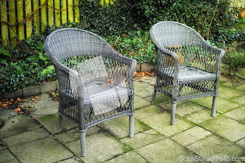 Image of Cozy garden area for coffee and reading outside in the warm summer. Two grey woven lawn chairs on a stone patio outside in an overgrown backyard. Old outdoor furniture in a private location to relax