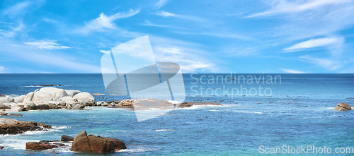 Image of Boulders at a beach against a cloudy blue sky background with copy space. Calm and majestic ocean across the horizon and rocky coast. Scenic landscape of the sea for a summer holiday or getaway