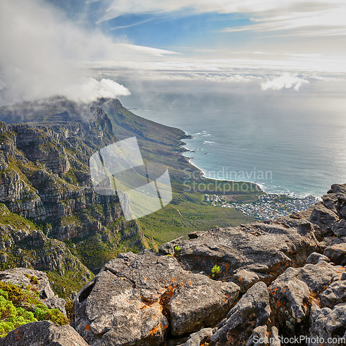 Image of Aerial view of a majestic mountain landscape, an ocean and a city in a valley during a cloudy day. Beautiful scenery of a cloudscaped sky above a rocky terrain with the sea below with copy space