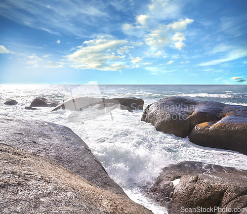 Image of Copy space ocean view of beach with foamy sea water crashing onto boulders and rocks on a peaceful summer vacation in South African. Texture and detail of scenic coastline and cloudy blue sky
