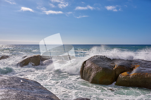 Image of Beautiful landscape view of the rough ocean waves breaking on large boulders with a blue sky background. Tidal waves crashing into rocks on the windy wild coast and beach of Cape Town, South Africa