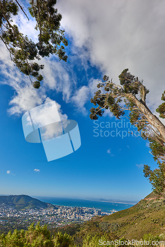 Image of Beautiful scenic view of a coastal city from a mountain peak with trees and plants against a cloudy blue sky background. Magnificent panoramic of a peaceful landscape at the sea to explore and travel