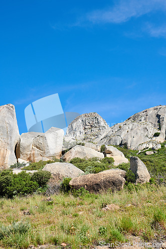Image of Copy space with rocks and boulders in rough hiking terrain with blue sky and copyspace. Lush green grass, wild shrubs and flora growing among stone monolith in a quiet nature reserve or countryside