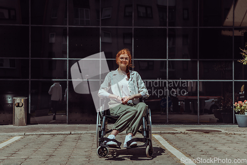 Image of In front of a modern corporate building, a young woman sitting in a wheelchair confidently, symbolizing empowerment, inclusivity, and the strength to overcome challenges in the business world