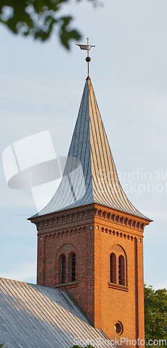 Image of Tall infrastructure and tower used to symbolize faith and Christian or Catholic devotion. Architecture roof design of church steeple and spire on gothic style cathedral building against blue sky.