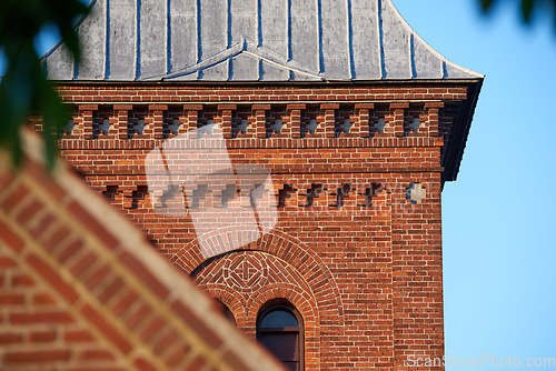 Image of Closeup of a red face brick church steeple against a blue sky. Tall infrastructure and tower used to symbolise faith and Christian or Catholic devotion. Architecture of a built structure outside