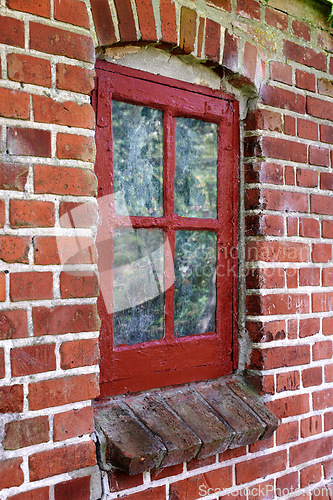 Image of Old dirty window in a brick wall house or home. Ancient casement with red wood frame on a historic building with a clumpy paint texture. Exterior details of a windowsill in a traditional country town