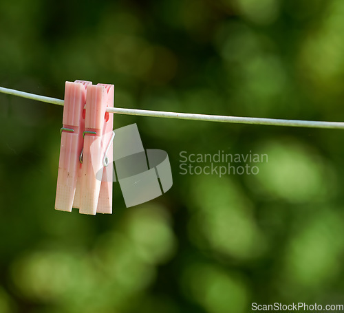 Image of Closeup of washing line with pins hanging outside against a bokeh green background. Empty clothesline with plastic clothes peg in a backyard on laundry day with copy space for domestic chores