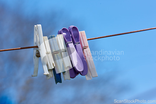 Image of Old washing line with broken pins hanging outside against a blurred blue background. Brown clothesline with different plastic pegs in a backyard on laundry day with copy space for domestic chores