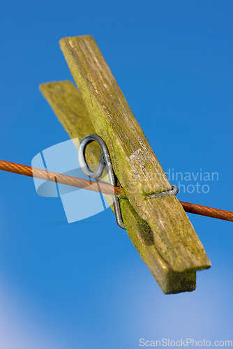 Image of Closeup of one clothes peg hanging on an empty laundry line outside in a garden. A clothing pin is a tool to hang up clothes outside to dry while doing housework and chores. Zoom of a wooden peg