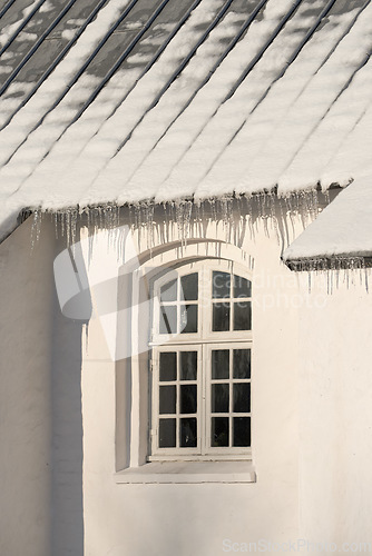 Image of Empty building with ice damming on the roof on a cold winter day. The exterior of a home or house with snow on the rooftop on a sunny afternoon. Frost on a historic church in a village