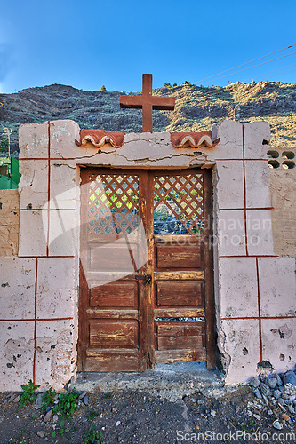 Image of Old abandoned church or cathedral with a weathered wall and broken wooden door. Vintage and aged religious building built in a traditional architectural style or design with a crucifix for faith