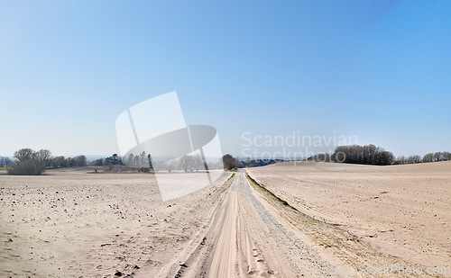 Image of A desolate agricultural farmland caused by summer heat droughts and impact on agriculture industry. Open and empty dry sand. Sandy and barren land with trees in the distance and blue sky background.