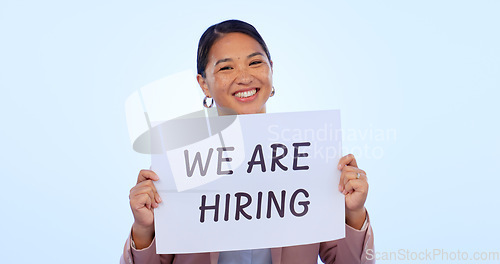 Image of Recruitment, smile and portrait of woman in a studio with a hiring sign, poster or board for job. Happy, employment and face of young Asian female person advertising a career offer by blue background