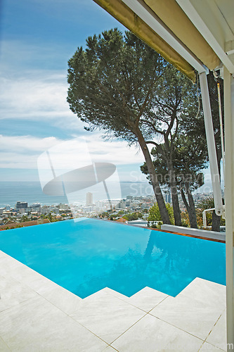 Image of Scenic view of infinity swimming pool overlooking city and ocean in background. Luxury outdoor blue pool on a tiled deck, patio and veranda of a condo, home or hotel. Cityscape and skyline with sea