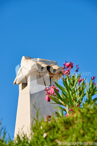 Image of Chimney tower designed roof house building outside against blue sky background and green plant foreground. Construction of exterior architecture of chute built on rooftop for fireplace smoke and heat