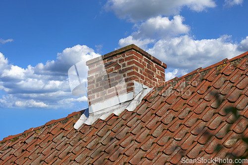 Image of Red brick chimney designed on slate roof of house building outside against blue sky with white clouds background. Construction of exterior escape chute built on rooftop for fireplace smoke and heat